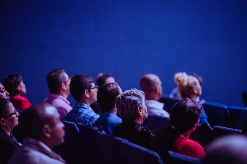 A group of friends sitting together on a cozy couch, enjoying a movie night. They are laughing and sharing snacks, with a large screen in front of them displaying a colorful film scene. The room is dimly lit, creating a warm and inviting atmosphere.