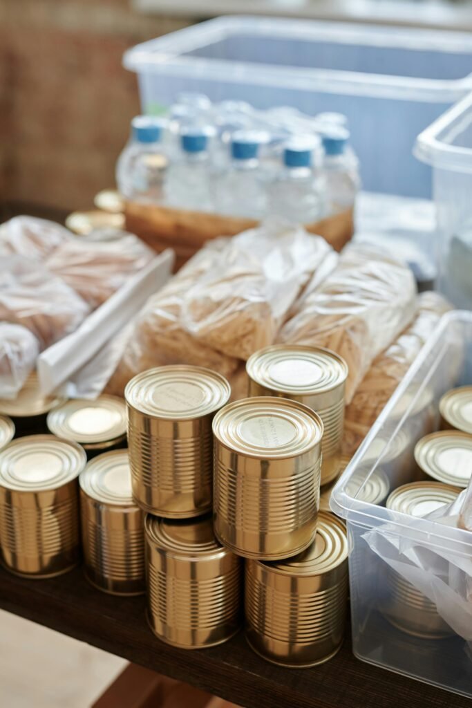 A community food drive scene with volunteers sorting and organizing canned goods and non-perishable food items on a long table. Bright autumn decorations, such as pumpkins and leaves, surround the area, creating a festive atmosphere. Volunteers of diverse backgrounds are actively engaged, smiling and working together to collect food donations for those in need. The setting reflects a sense of community spirit and collaboration during the fall season.