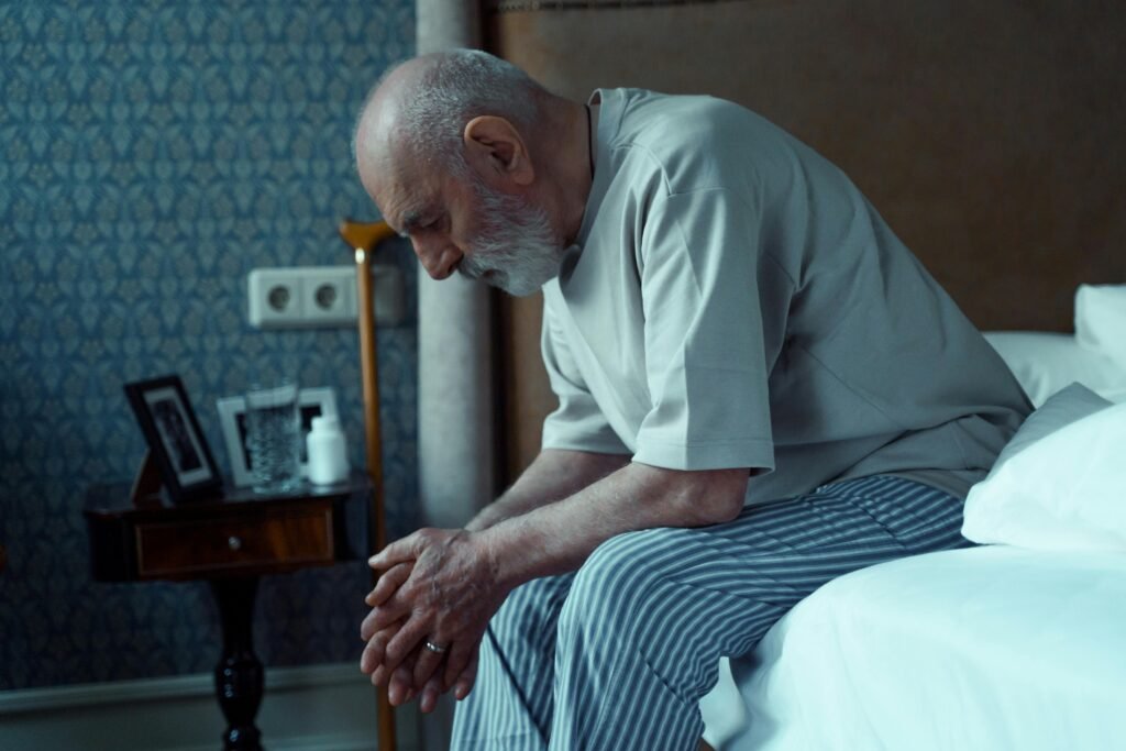 an old man sitting in his bed with the head down