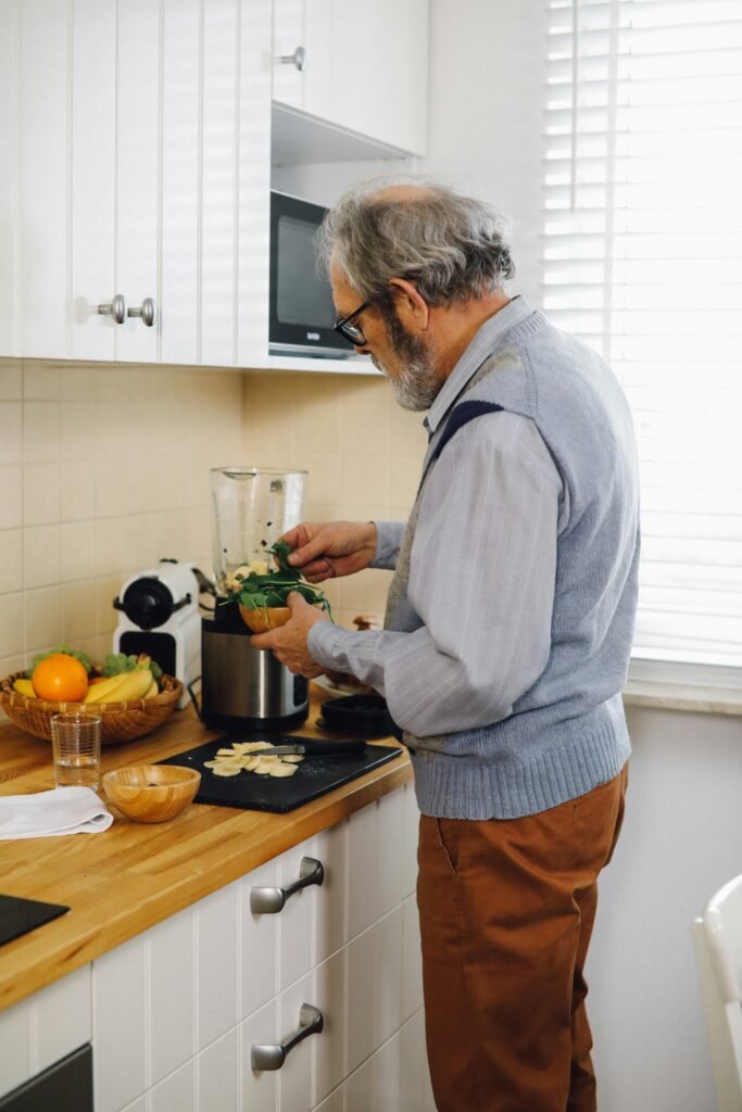 An elderly man chopping vegetables on a kitchen counter, preparing ingredients for cooking. The kitchen is warm and inviting, with fresh produce and cooking tools neatly arranged around him.