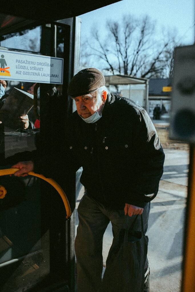 "An elderly man boarding a bus for a day trip, smiling as he holds onto the handrail. He’s dressed comfortably, with a backpack slung over his shoulder, ready for a day of adventure."