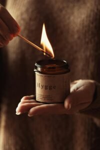 A warm, autumn-scented candle with a pumpkin spice fragrance surrounded by fall leaves, cinnamon sticks, and a cozy sweater, creating a festive, seasonal ambiance perfect for autumn.