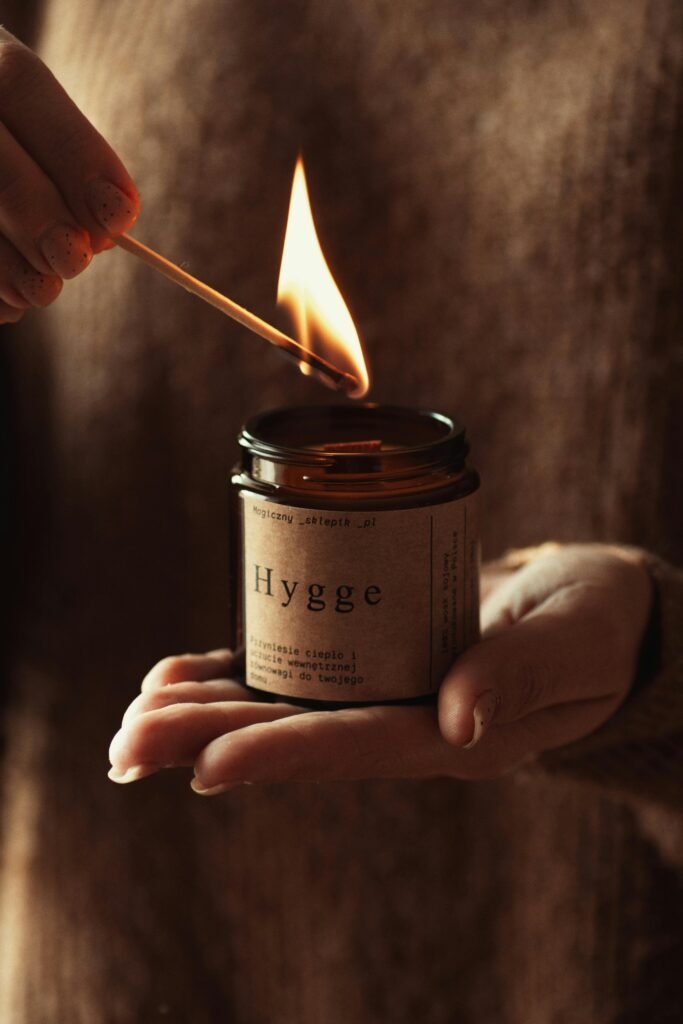 A warm, autumn-scented candle with a pumpkin spice fragrance surrounded by fall leaves, cinnamon sticks, and a cozy sweater, creating a festive, seasonal ambiance perfect for autumn.