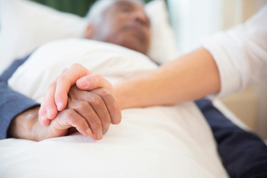 someone holding the hand of an elder man laying in bed