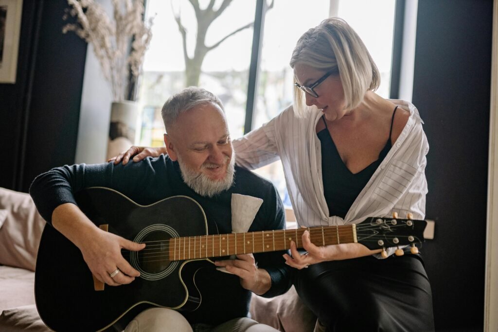old man learning how to play the guitar with his wife
